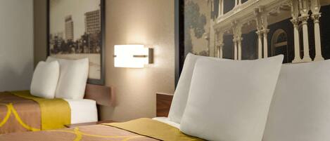 A hotel room with a bed, pillows, a headboard, and a wall-mounted light fixture.