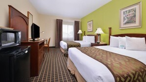 Ein Hotelzimmer mit einem Bett, zwei Nachttischen, einem Schreibtisch mit Computer, einem Fernseher und einer Mikrowelle.