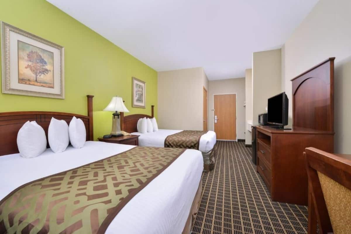 A hotel room with two beds, a desk, a television, and a door leading to another room.