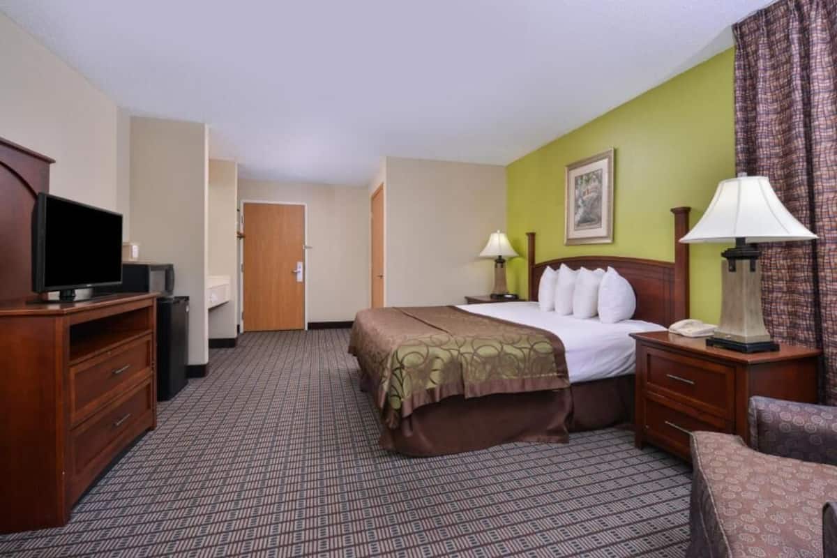 A hotel room with a bed, bedside tables, a desk with a television, and a lamp.