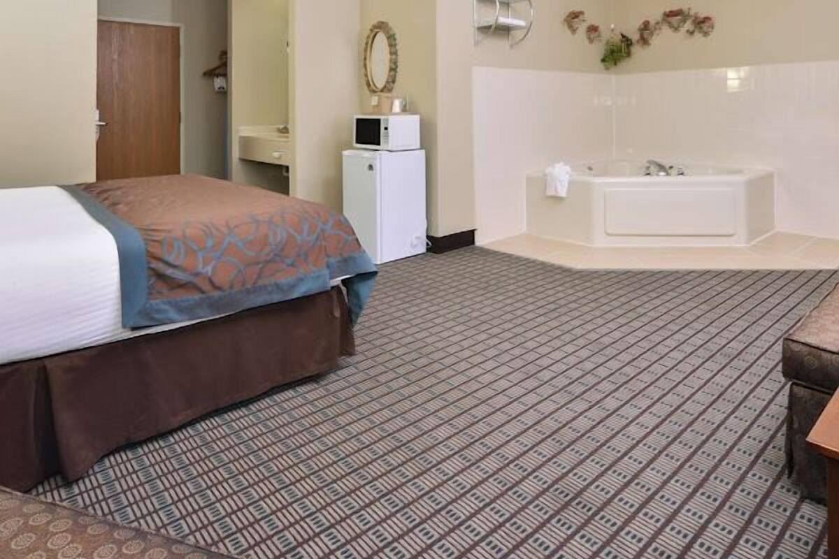 A hotel room with a bed, a small desk, a microwave, a mirror, a wall-mounted towel rack, and a bathtub.