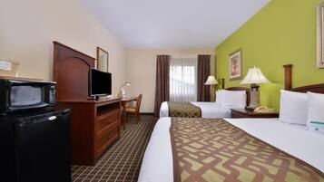 A hotel room with a bed, a desk with a television, a microwave, a lamp, and a telephone.
