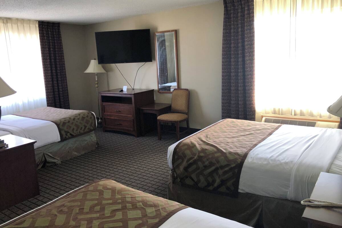 A hotel room with two beds, a desk, a chair, a TV, and a window with curtains.