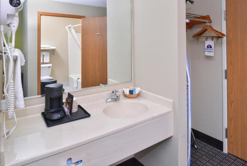 A hotel bathroom with a large mirror, a sink, a hairdryer, and a coffee maker.