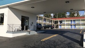 A motel with a covered parking area, a two-story building with a red roof, and a black car parked in front. - American INN of Orangeburg (Orangeburg)