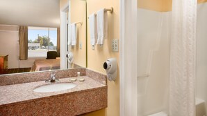 A hotel bathroom with a granite countertop sink, a mirror, a towel rack, and a shower curtain. - American INN of Orangeburg (Orangeburg)