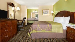 A hotel room with a bed, a desk with a chair, a dresser, a television, and a bathroom visible through an open door. - American INN of Orangeburg (Orangeburg)