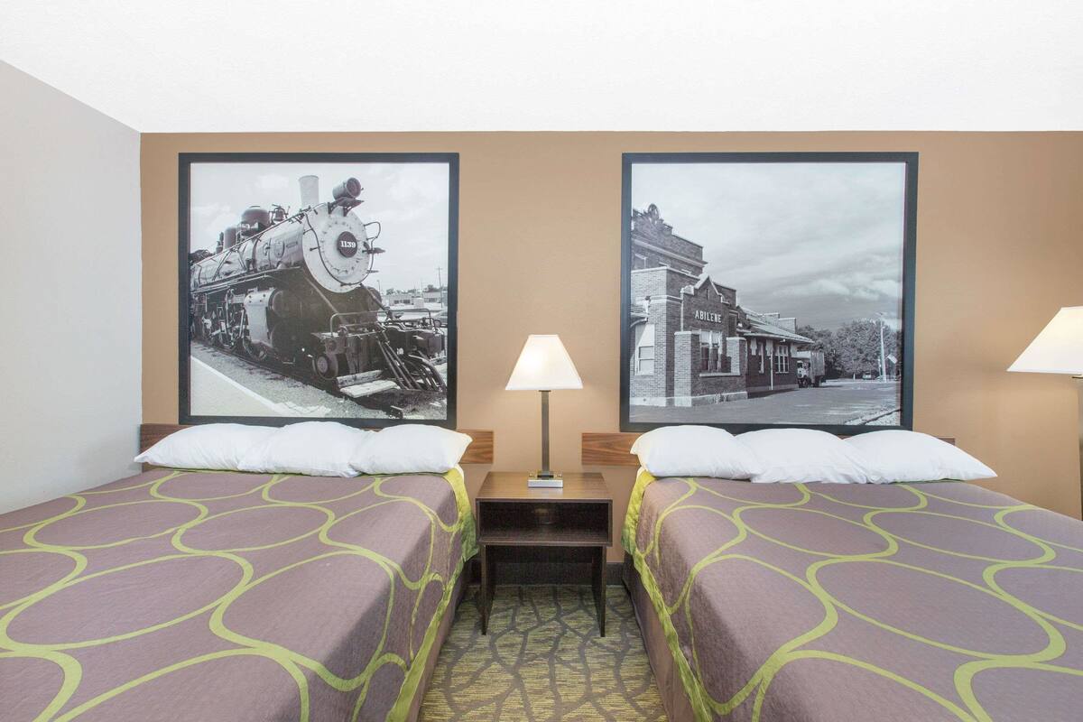 A hotel room with two beds, a nightstand, a lamp, and two framed pictures on the wall.