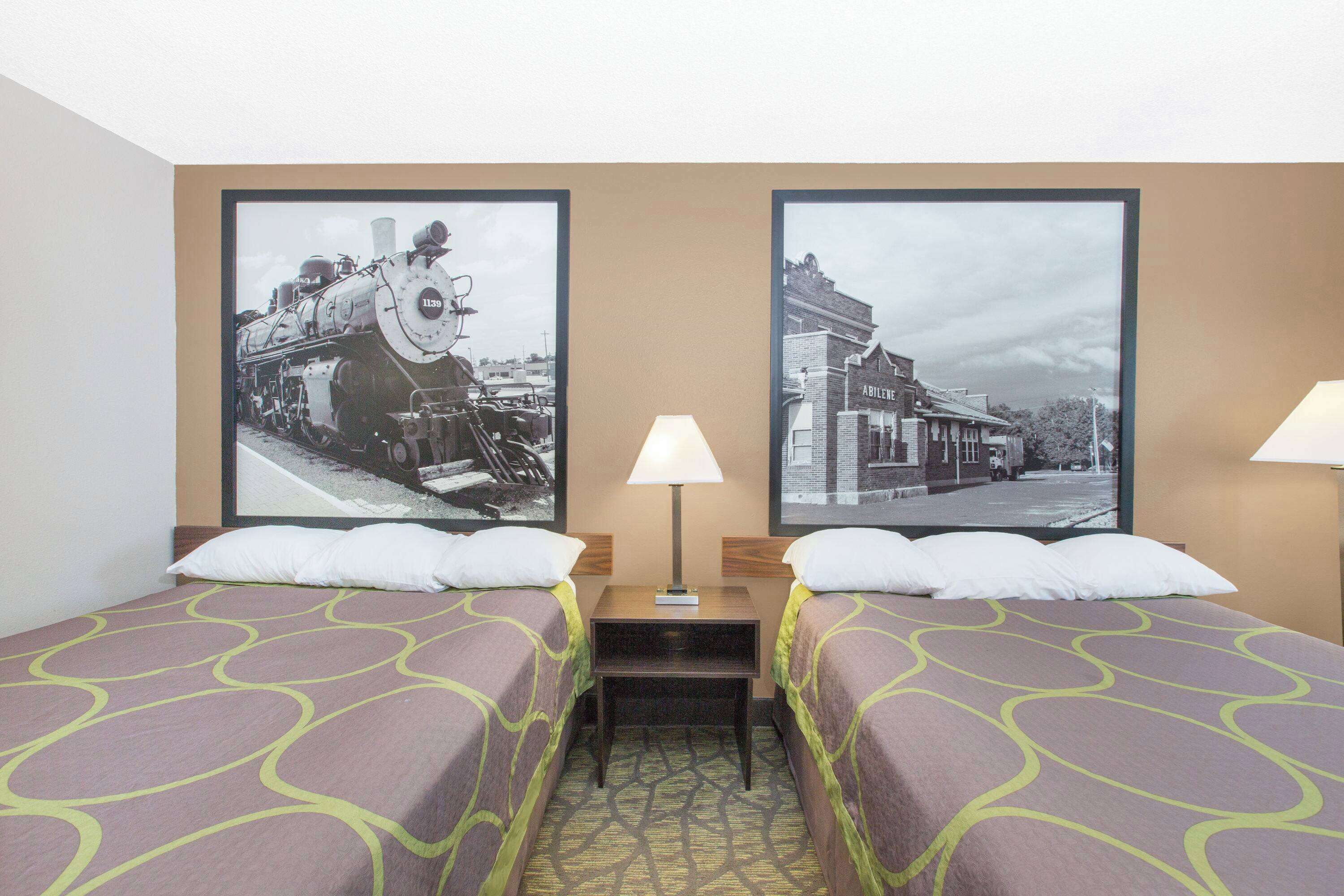 Ein Hotelzimmer mit zwei Betten, einem Nachttisch und zwei Lampen. An der Wand befinden sich zwei gerahmte Bilder.