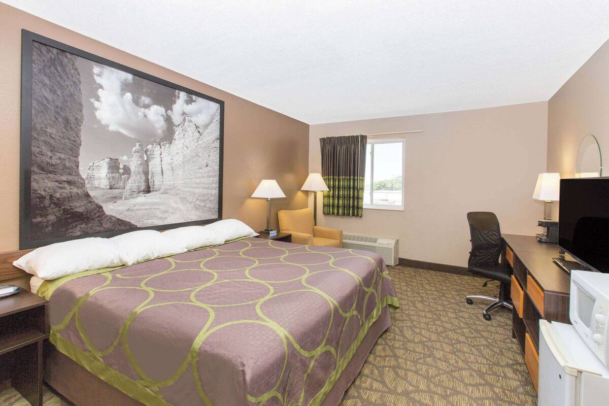 A hotel room with a large bed, two bedside lamps, a desk with a computer, and a television.