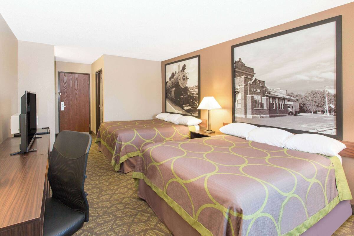 A hotel room with two beds, a desk, a chair, and a television.