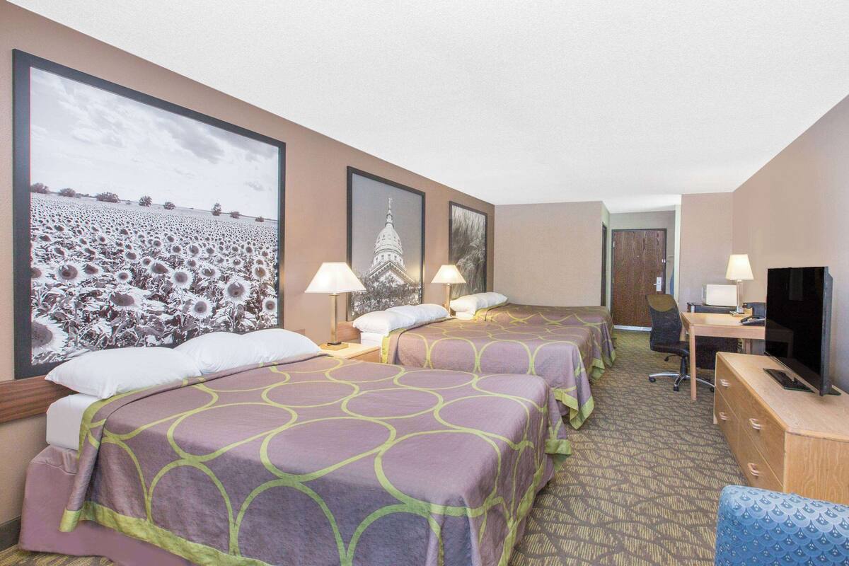 A hotel room with two beds, a desk, a chair, a television, and framed pictures on the walls.