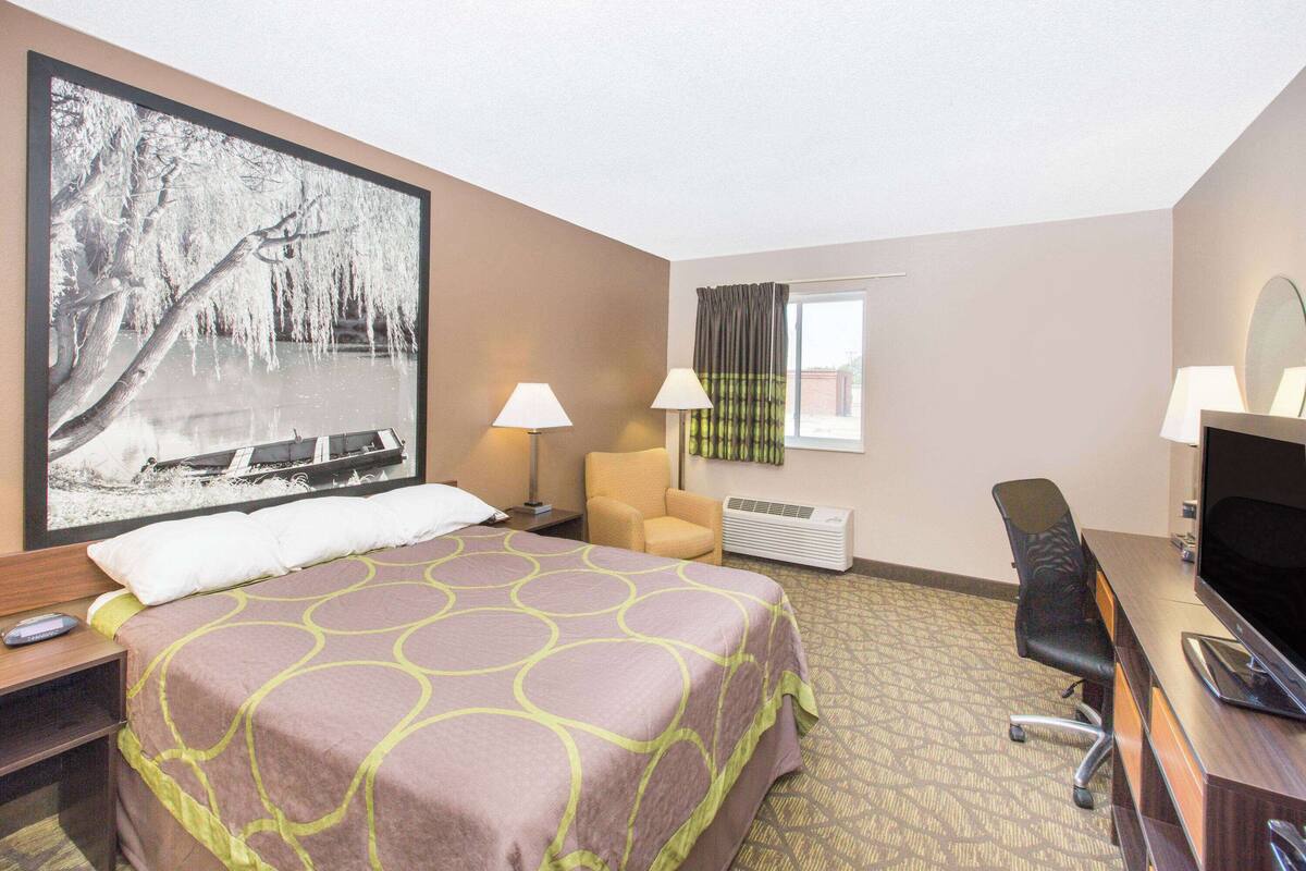 A hotel room with a large bed, a desk with a computer, a chair, a TV, and a window with curtains.