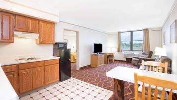 Habitación de hotel con kitchenette, zona de comedor, televisor, sofá y ventana grande.