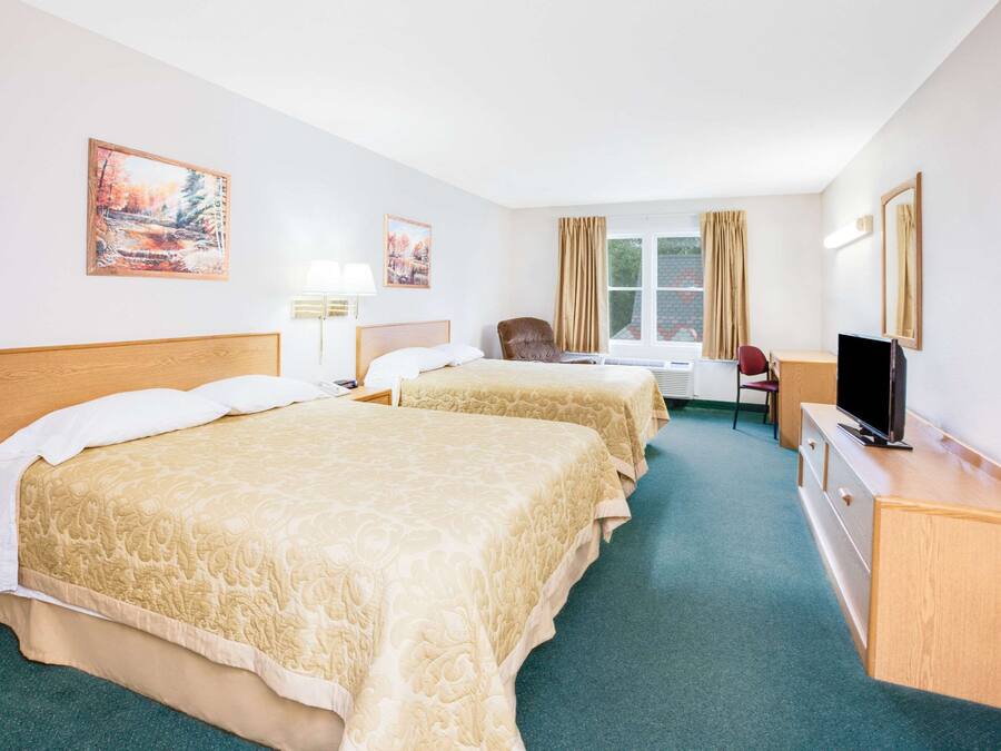 A hotel room with two beds, a desk, a chair, a TV, and artwork on the walls.