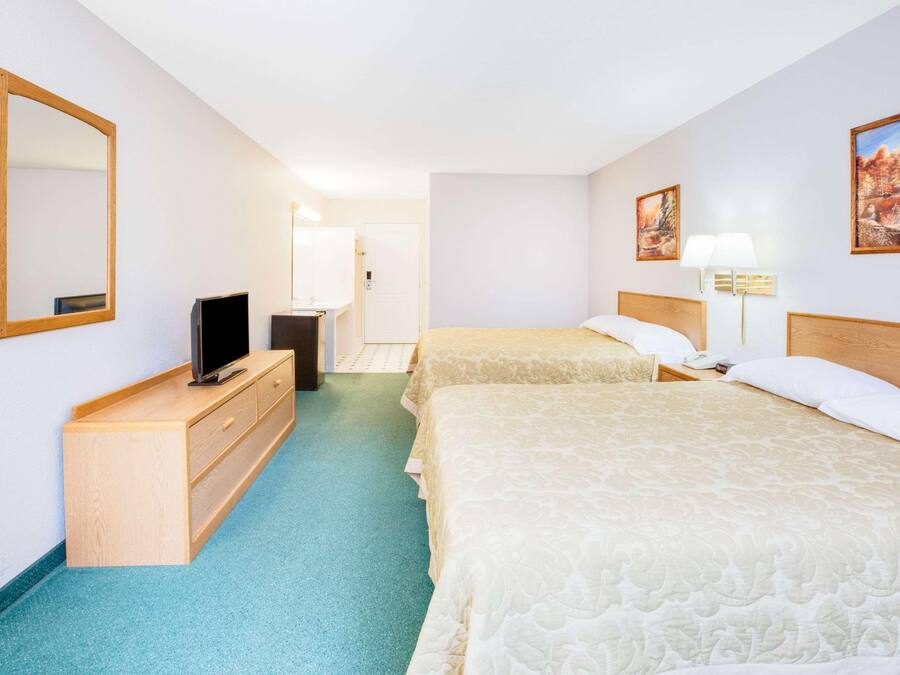 Habitación de hotel con dos camas, televisión, cómoda y puerta de baño.