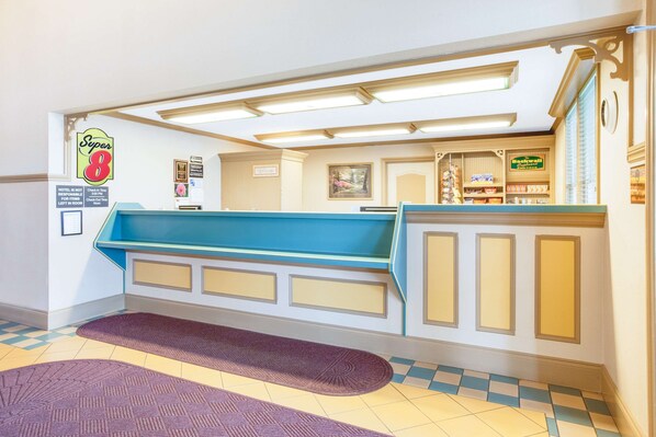 Een hotel receptie met een incheckbalie, een bord met 'Super 8' en een 'Backwall' bord dat een achtergebied aangeeft.