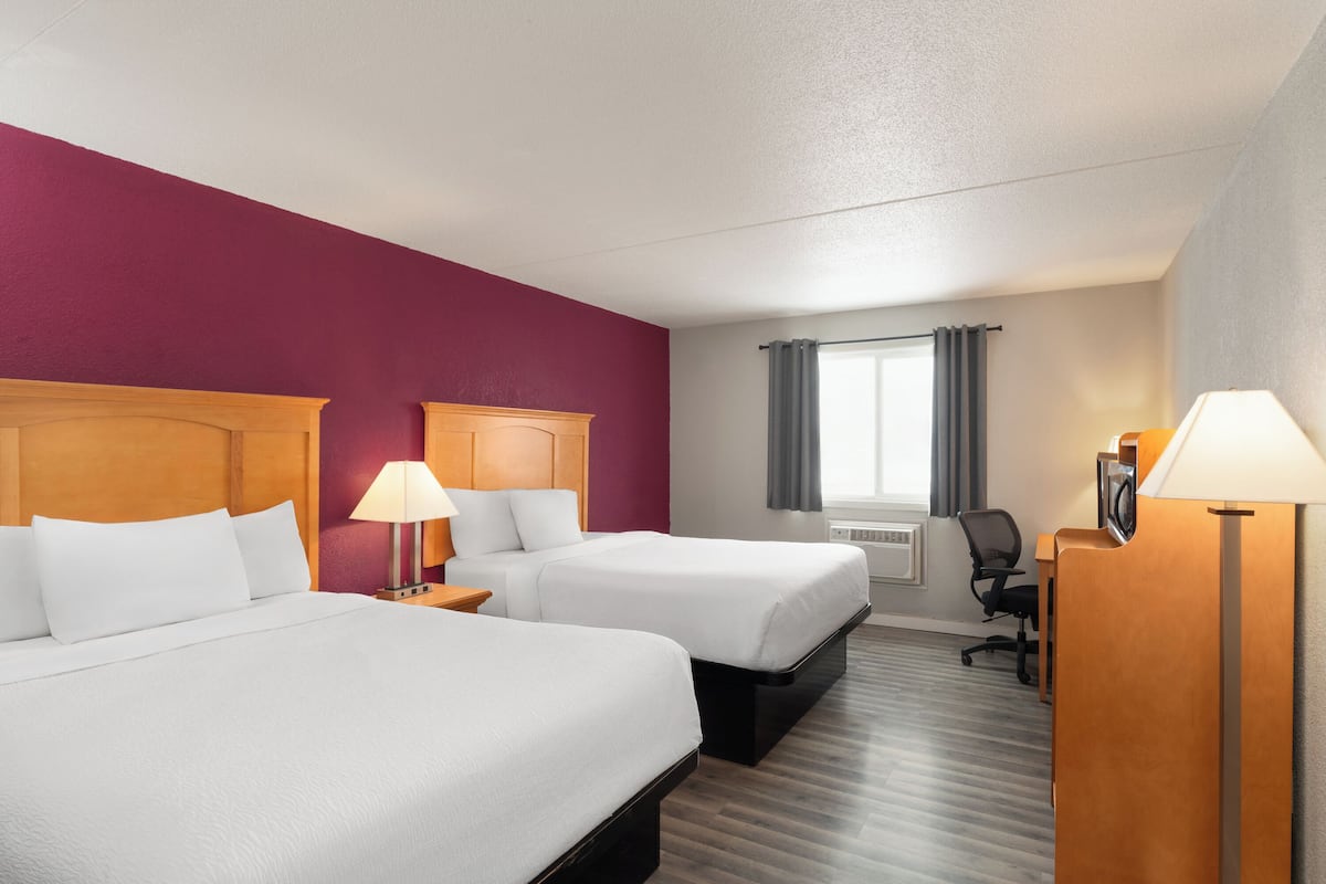 Habitación de hotel con dos camas, un escritorio, una silla y una ventana con cortinas.
