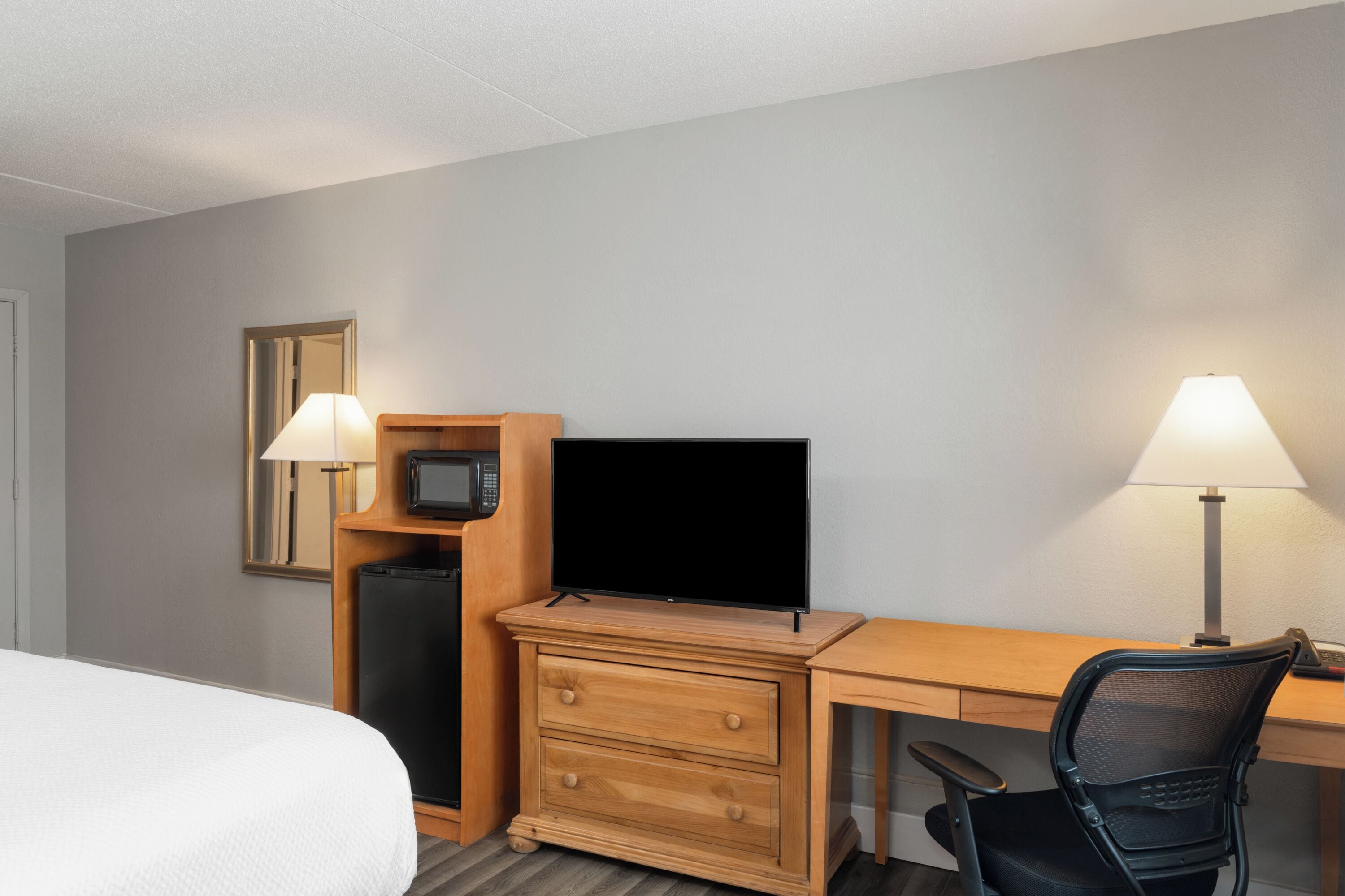 A hotel room with a bed, a desk with a computer, a TV, a microwave, and two lamps.