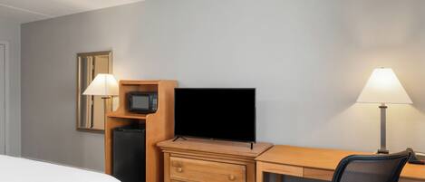 A hotel room with a bed, a desk with a computer, a TV, a microwave, and two lamps.