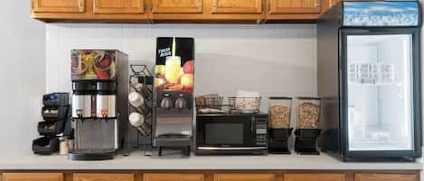 Una cocina con gabinetes de madera, cafetera, microondas, licuadora y refrigerador.