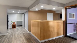 A reception area with a wooden reception desk, a potted plant, and a door leading to another room. - Sauk River Inn & Suites, a Travelodge by Wyndham (Sauk Centre)