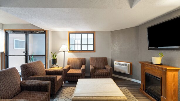 A living room with a fireplace, two armchairs, a sofa, a coffee table, a TV, and a window with blinds. - Sauk River Inn & Suites, a Travelodge by Wyndham (Sauk Centre)
