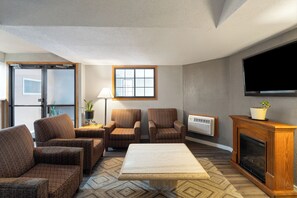 A living room with a fireplace, two armchairs, a sofa, a coffee table, a TV, and a window with blinds. - Sauk River Inn & Suites (Sauk Centre)