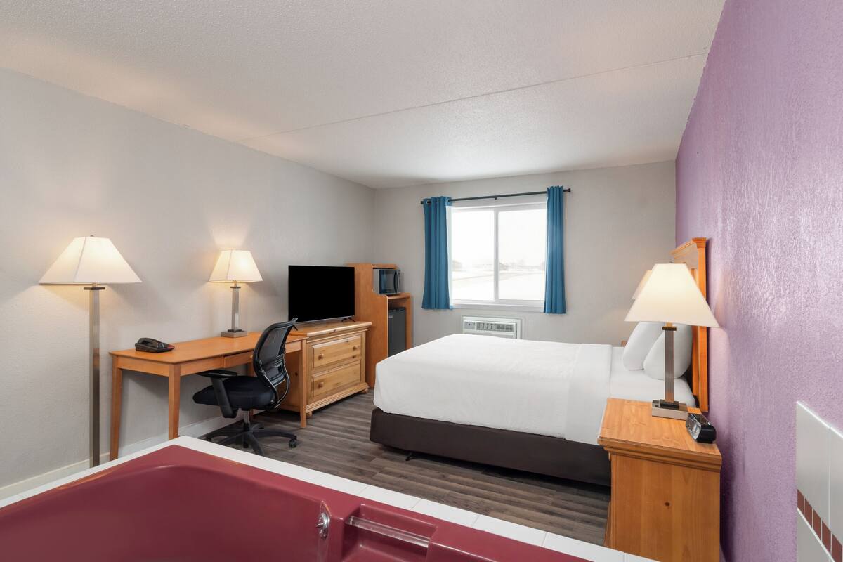 Una habitación de hotel con cama, escritorio, silla, televisor y bañera.