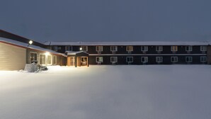 A building with a snow-covered ground, multiple windows, and a well-lit entrance. - Sauk River Inn & Suites, a Travelodge by Wyndham (Sauk Centre)