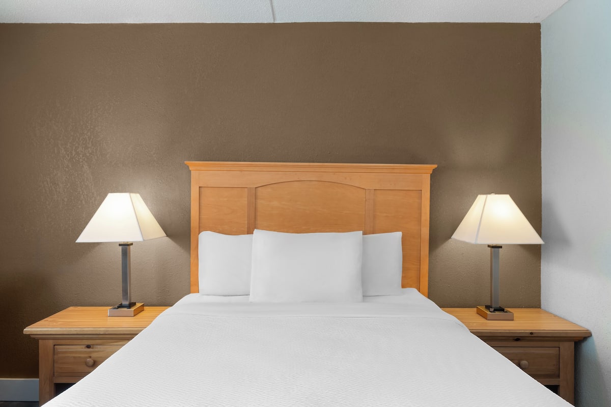 Una cama bien hecha con sábanas blancas, flanqueada por dos mesitas de noche con lámparas, frente a una pared marrón.