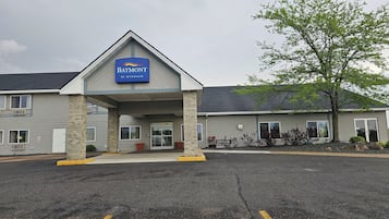 Hotel Baymont by Wyndham con entrada techada, estacionamiento y un árbol en la fachada.