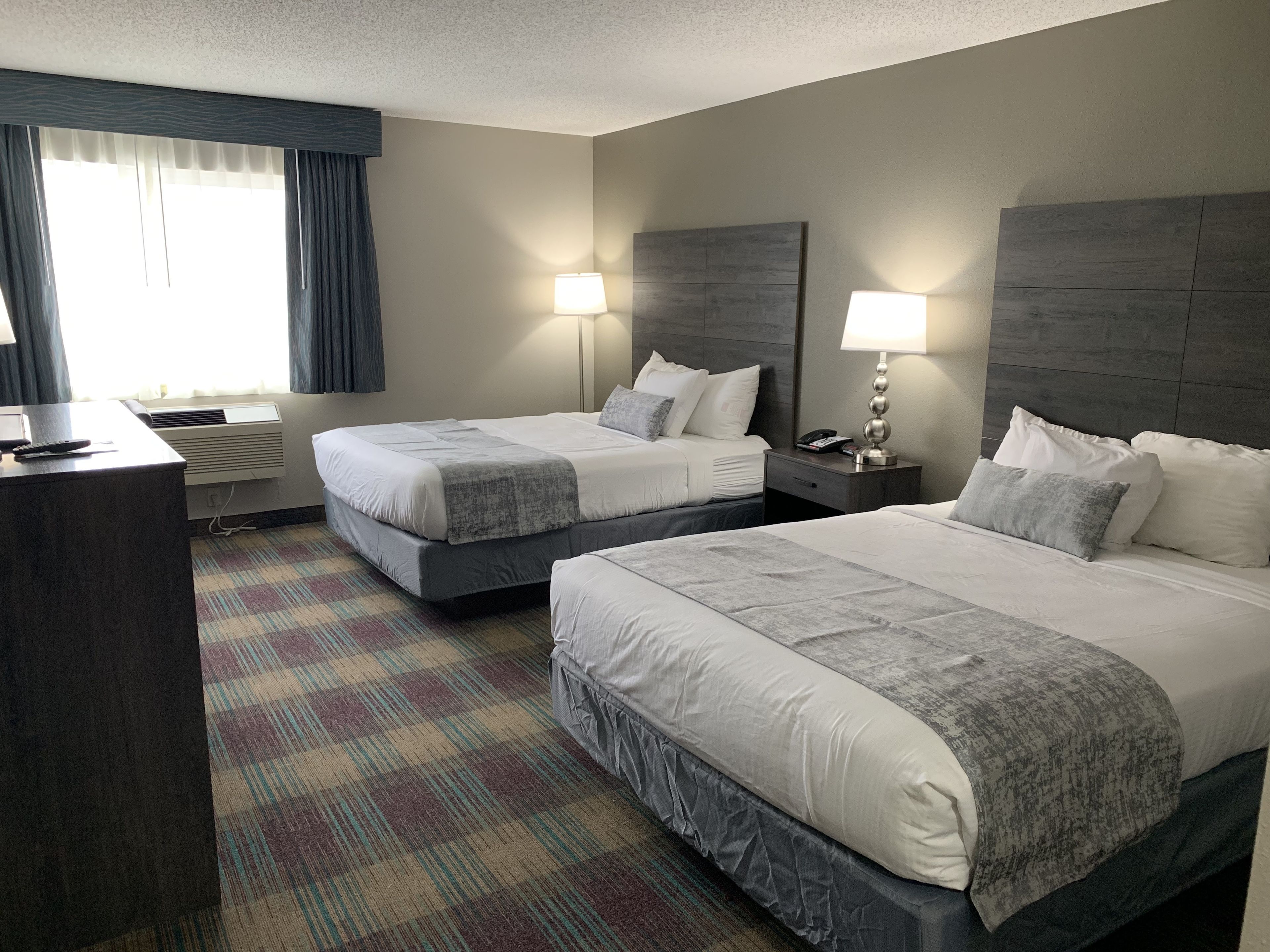 A hotel room with two beds, a desk, and a window with curtains.