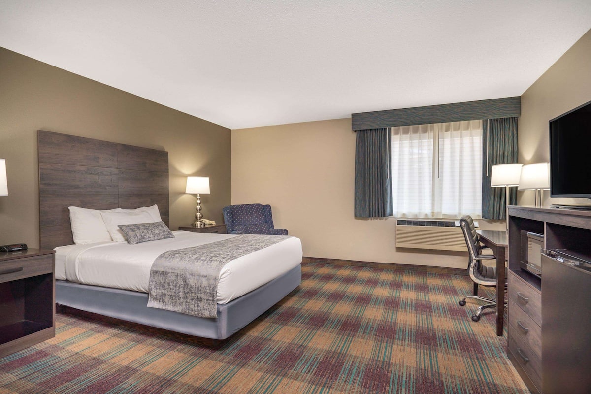 A hotel room with a large bed, a desk, a chair, a TV, and a window with curtains.