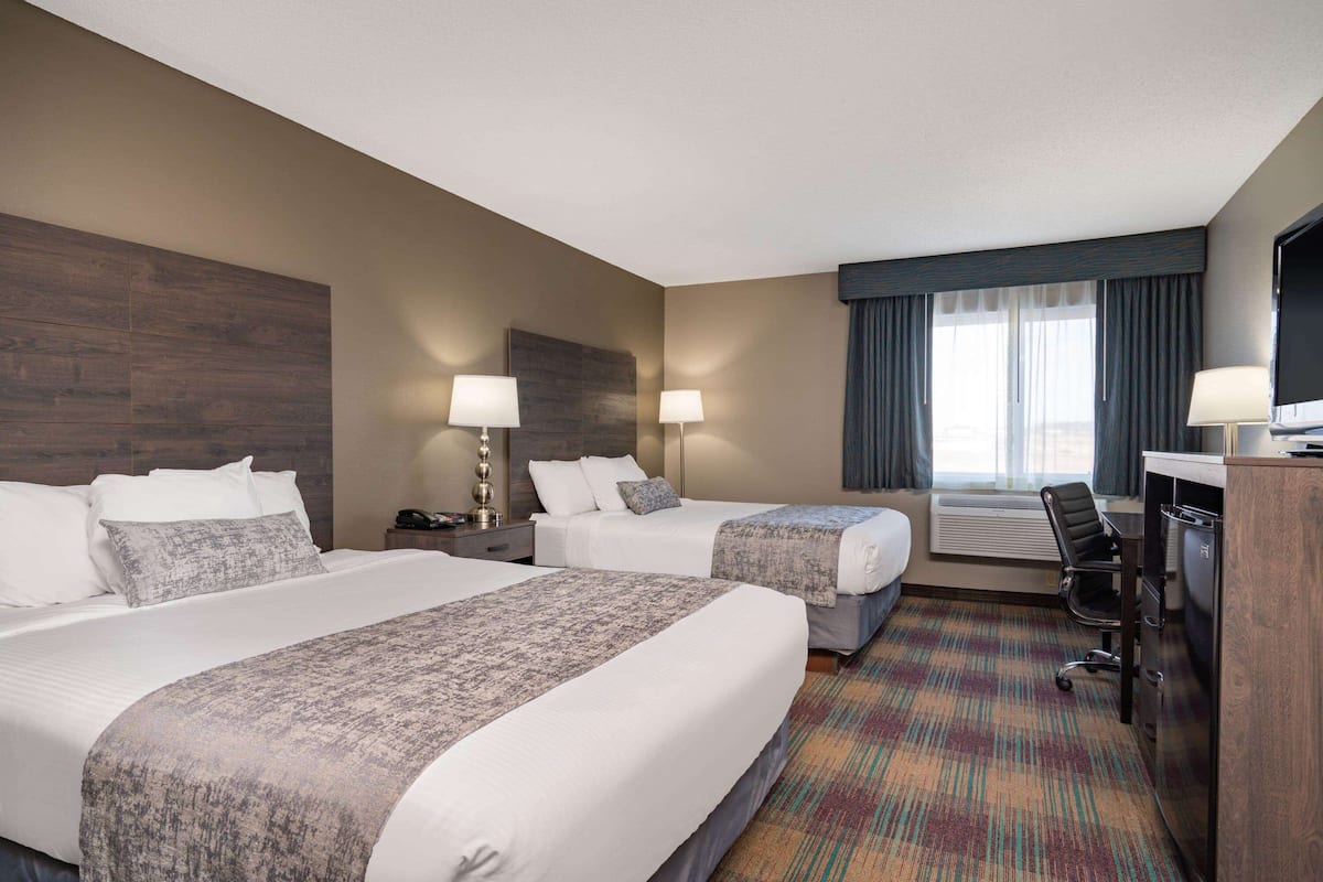 A hotel room with two beds, a desk, a chair, a TV, and a large window with curtains.