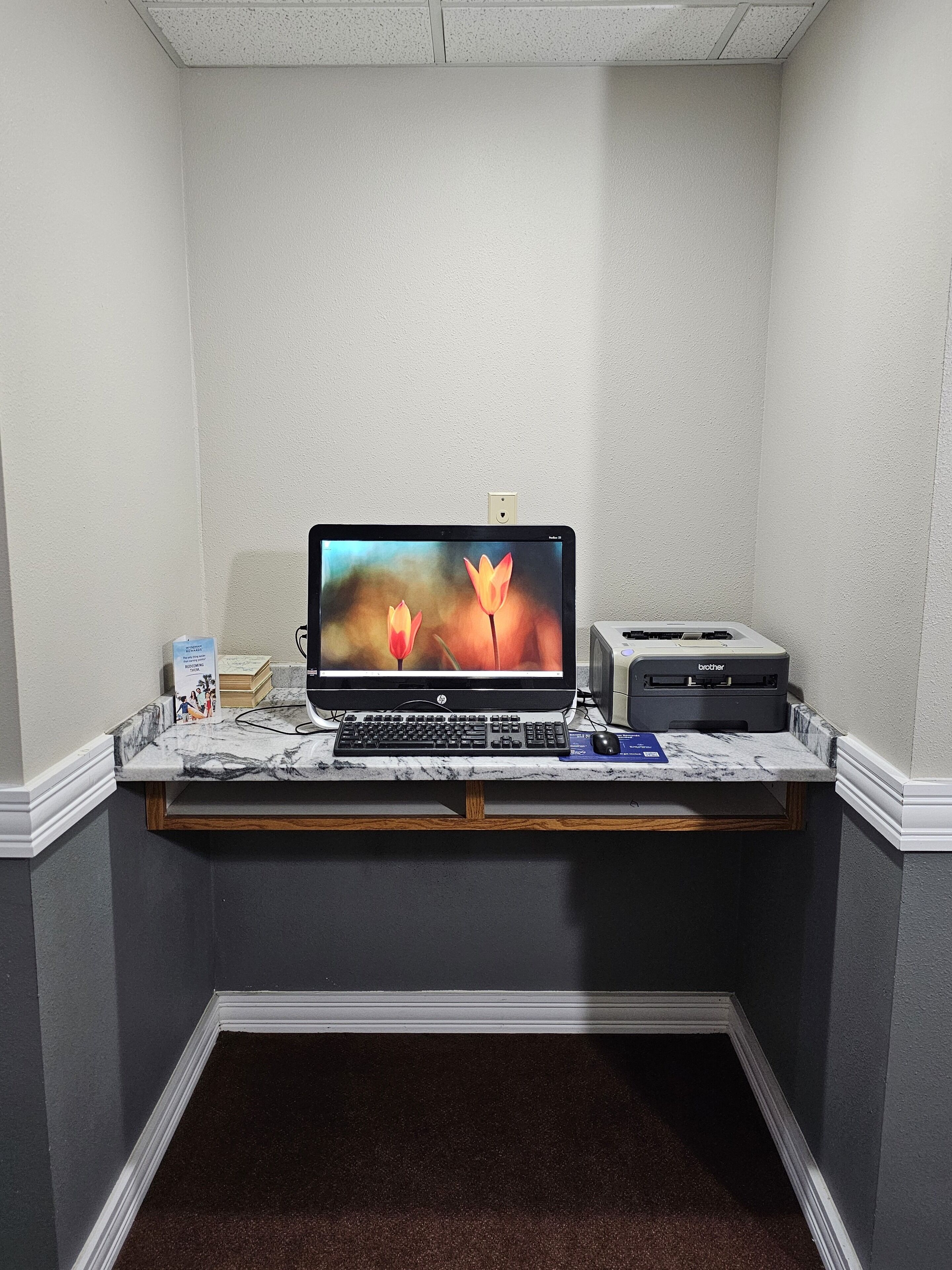 A computer desk with a monitor, keyboard, and printer in a corner room.