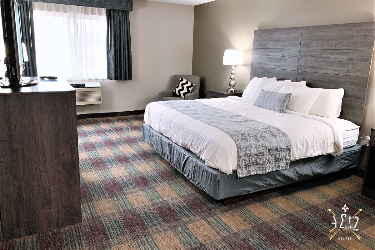 A hotel room with a large bed, a desk, a chair, a lamp, and a window with curtains.