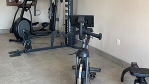 Une salle de sport à domicile équipée d’un vélo elliptique, d’un vélo d’appartement et d’une machine de musculation.