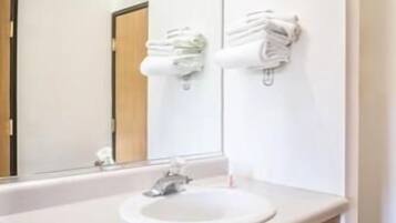 Un baño con lavamanos, espejo y dispensador de toallas.