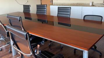 A conference room with a long wooden table, black leather chairs, and a white kitchenette in the background.