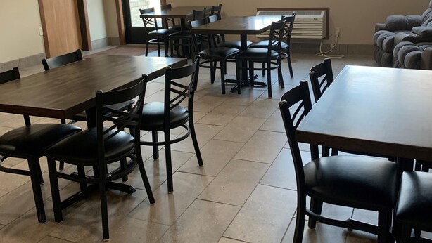 Un espace repas comprenant plusieurs tables et chaises, une porte avec un panneau indiquant la sortie, et une fenêtre donnant sur l’extérieur.