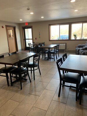 A dining area with multiple tables and chairs, a door with an exit sign, and a window with a view of the outside. - Super 8 by Wyndham Phillips (Phillips)