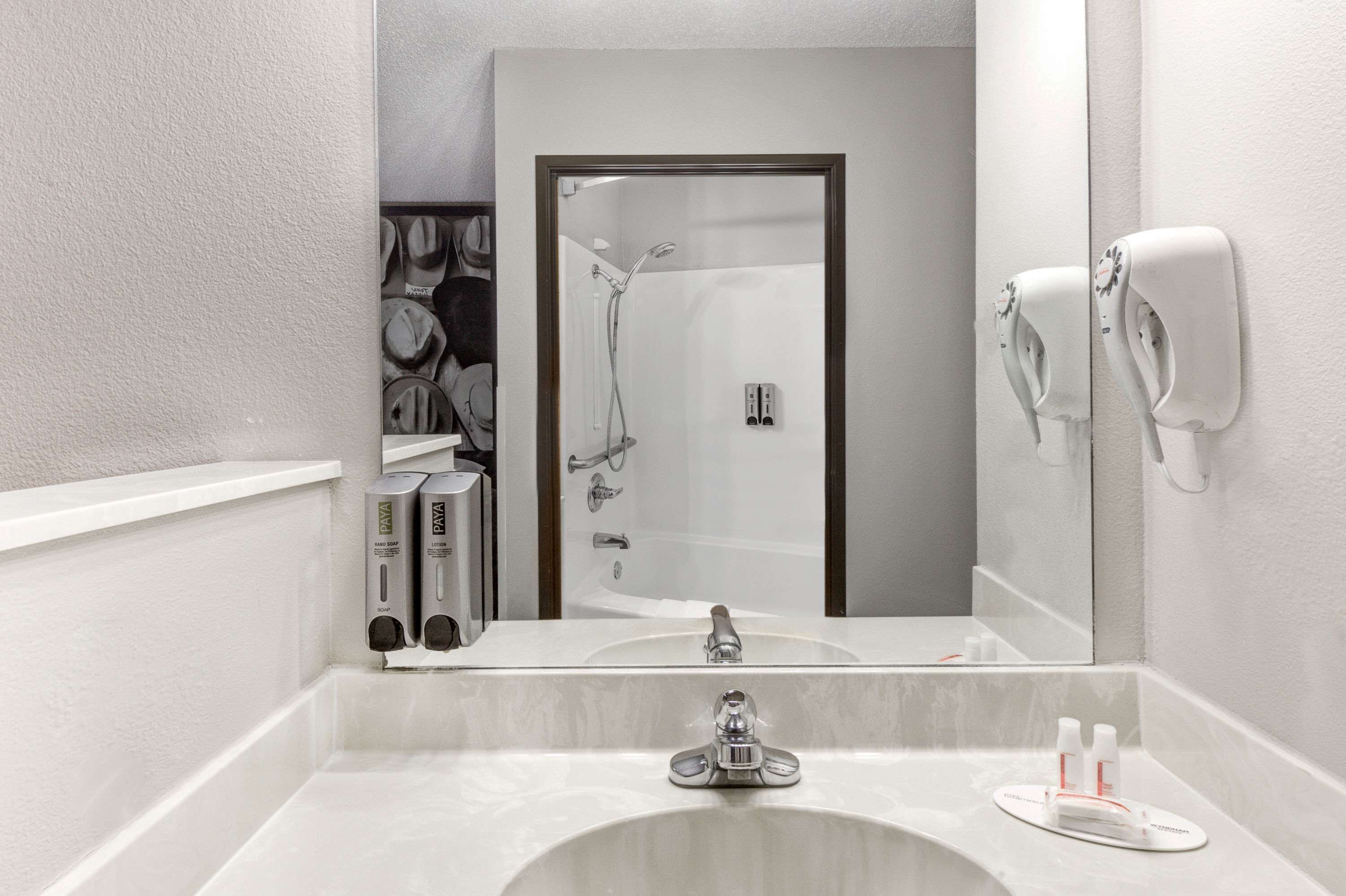 A modern bathroom with a large mirror, a sink, a shower, and a towel dispenser.
