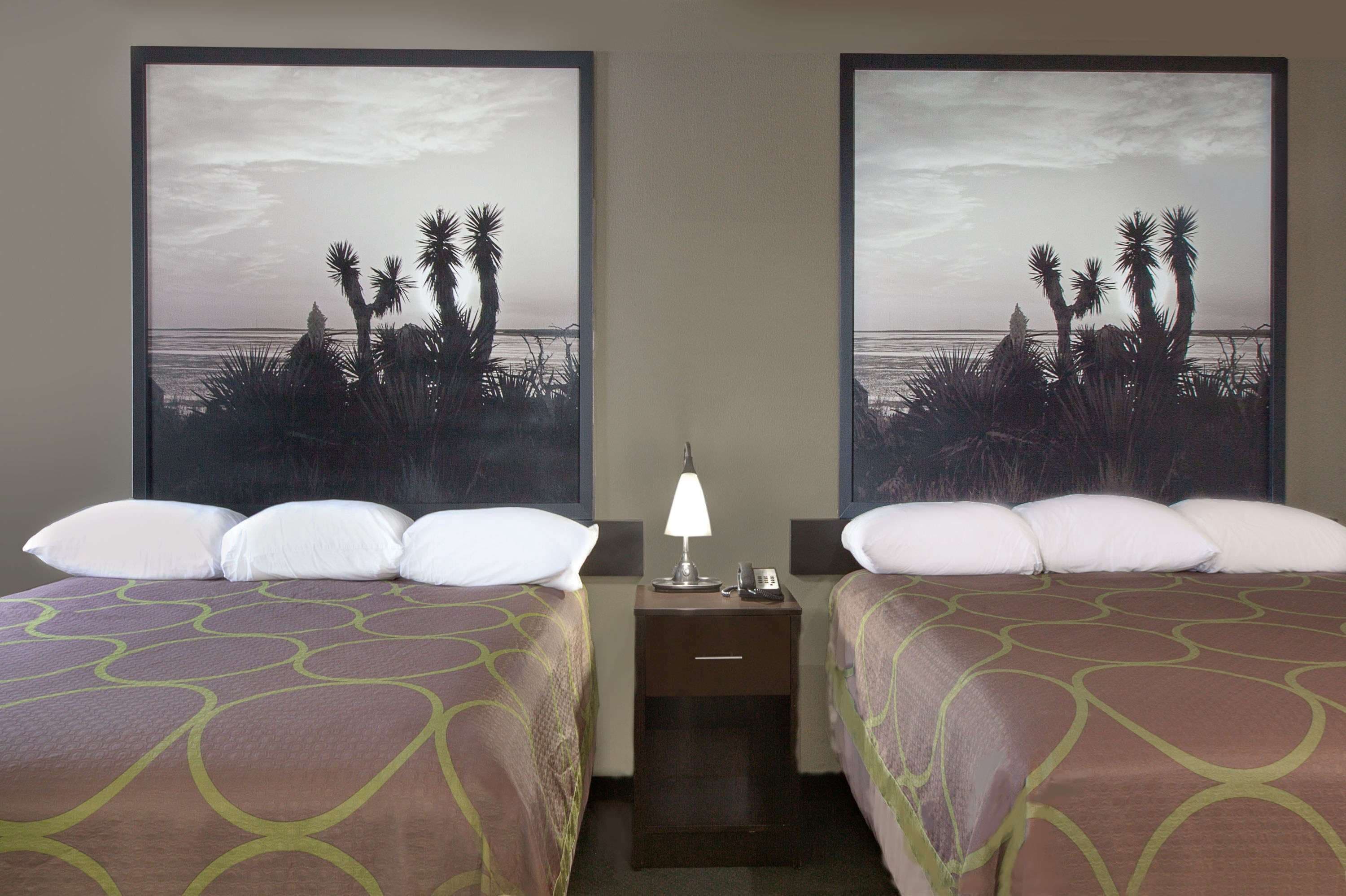 A hotel room with two beds, a nightstand with a lamp, and a large framed picture of a beach scene.