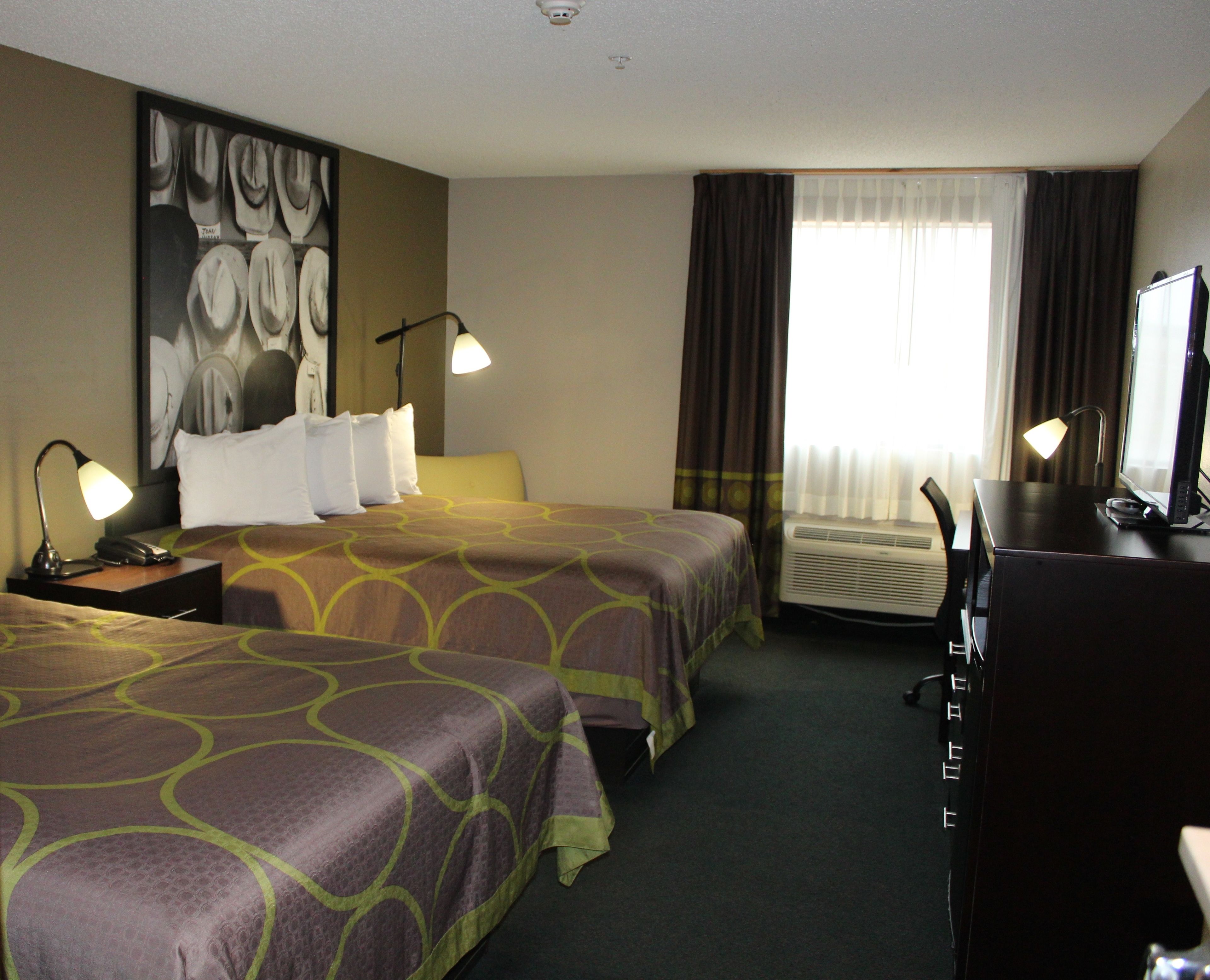 Quarto de hotel com duas camas, uma mesa, uma cadeira, luminária de mesa, telefone e ar condicionado.