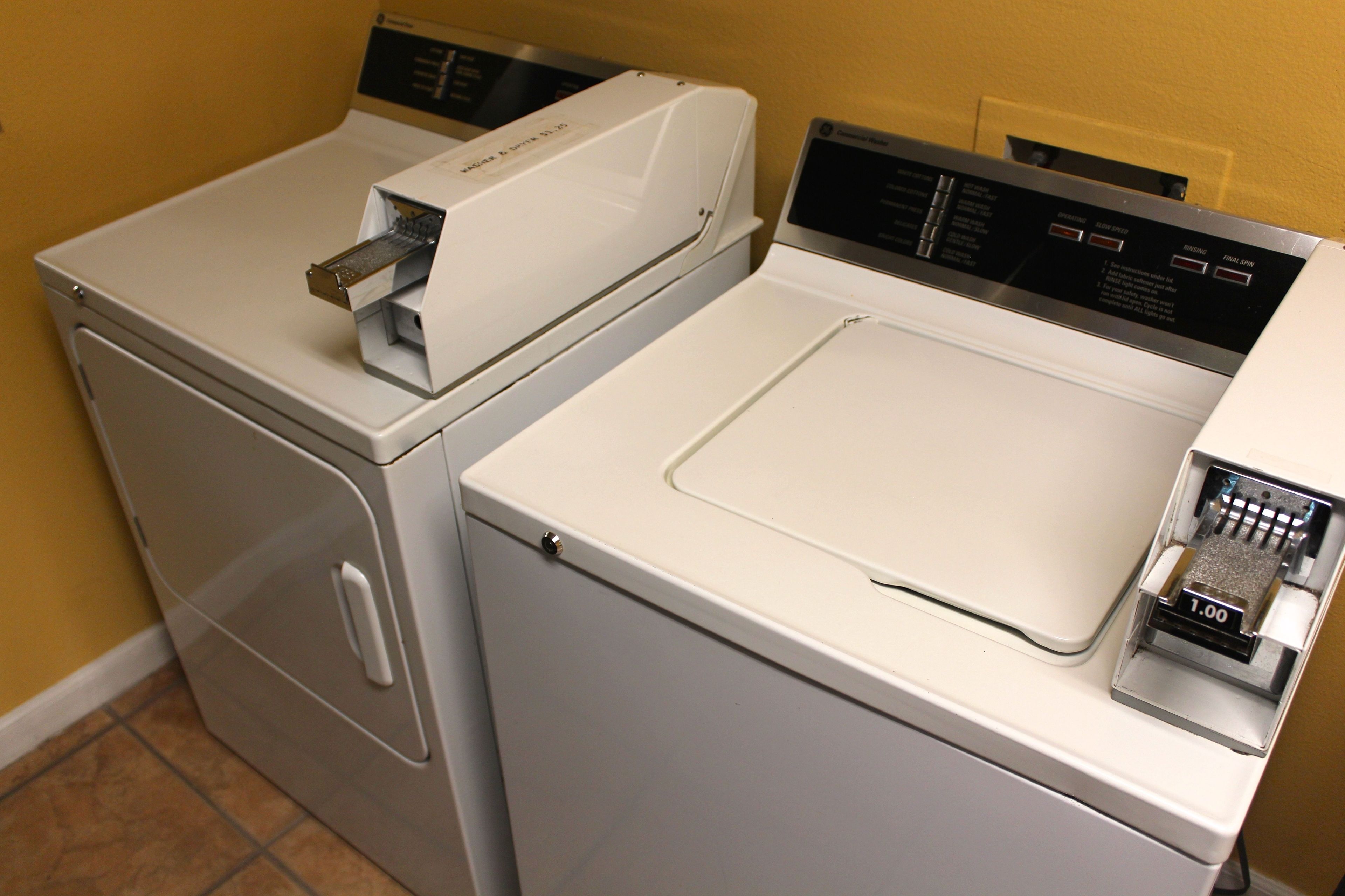 Une buanderie moderne et compacte, équipée de deux machines à laver et deux sèche-linge superposés, dotée de panneaux de commande numériques et d’un sèche-linge à pièces.