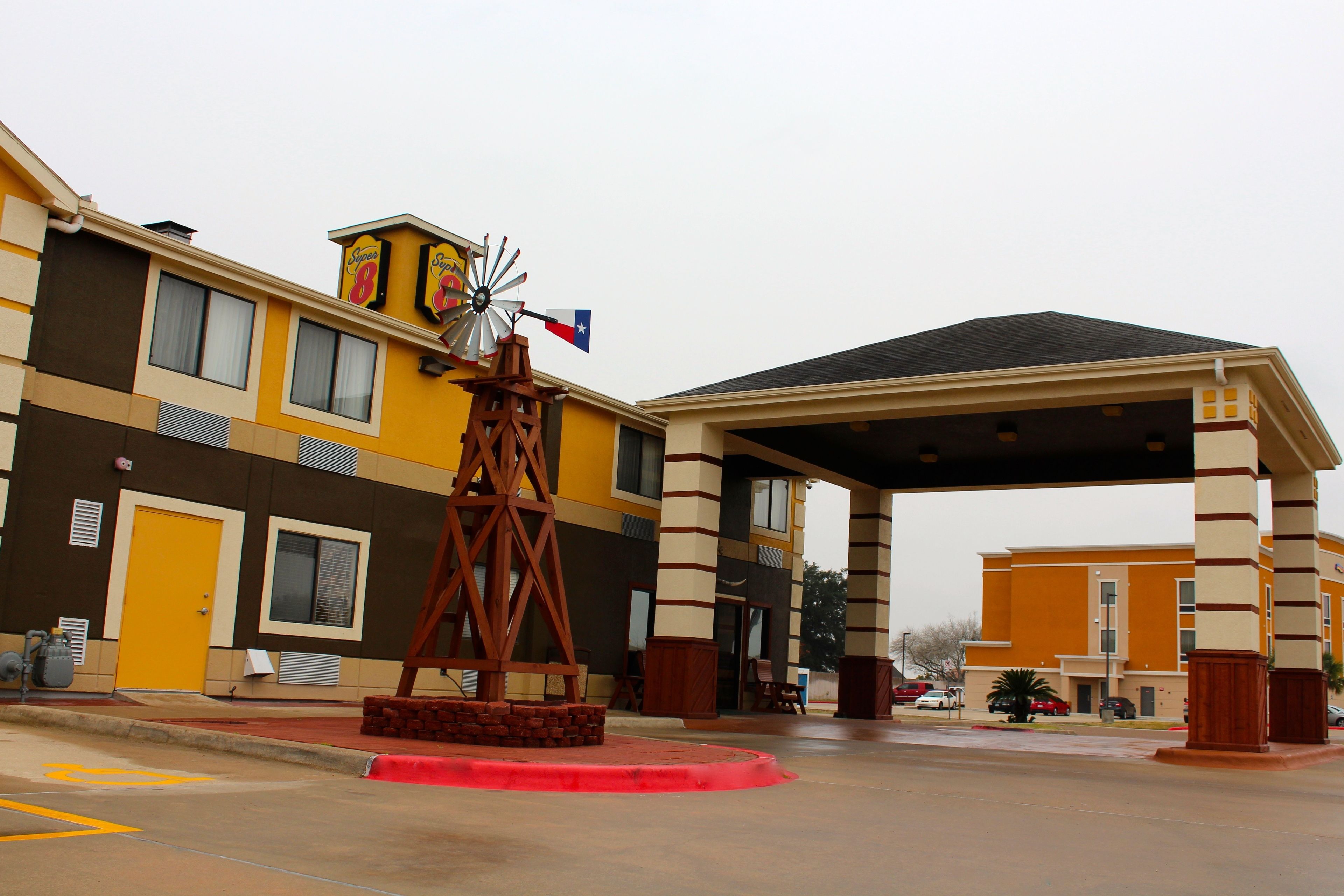A hotel entrance with a windmill, a covered waiting area, and a parking lot.