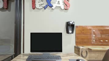 Un espacio de trabajo con un monitor de computadora, teclado y ratón sobre un escritorio de madera. Se ve un altavoz montado en la pared, y una señal decorativa con la palabra “TEXAS” está sobre el monitor.