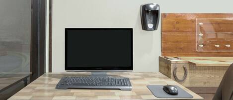 A workspace with a computer monitor, keyboard, and mouse on a wooden desk. A wall-mounted speaker is visible, and a decorative sign spelling "TEXAS" is above the monitor.