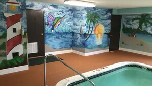 Une piscine ornée d’une fresque représentant un paysage tropical, un poste de surveillance pour les sauveteurs et une signalétique indiquant l’emplacement du local technique.